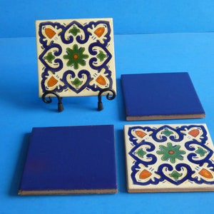 May include: Four square ceramic tiles, two with a blue glaze and two with a white background and a colorful floral pattern. The tiles are arranged in a row on a blue surface.