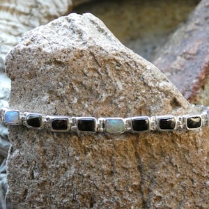 May include: A silver bracelet with alternating black and white rectangular stones. The bracelet is made of sterling silver and features a delicate chain link design.
