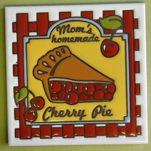 May include: A yellow and red ceramic tile with a picture of a cherry pie. The tile has the text "Mom's homemade Cherry Pie" on it.