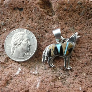 May include: Sterling silver pendant featuring a wolf howling, inlaid with turquoise, black onyx, and other stones. The pendant is about the size of a quarter.