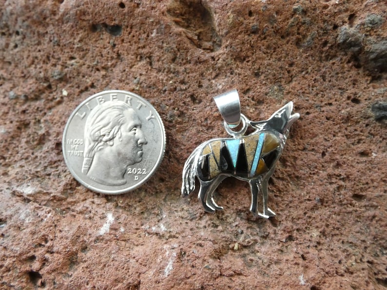 May include: Sterling silver pendant featuring a wolf howling, inlaid with turquoise, black onyx, and other stones. The pendant is about the size of a quarter.