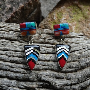 May include: A pair of dangle earrings with a geometric design. The earrings are made of silver and feature a variety of colorful stones, including turquoise, red coral, and black onyx.