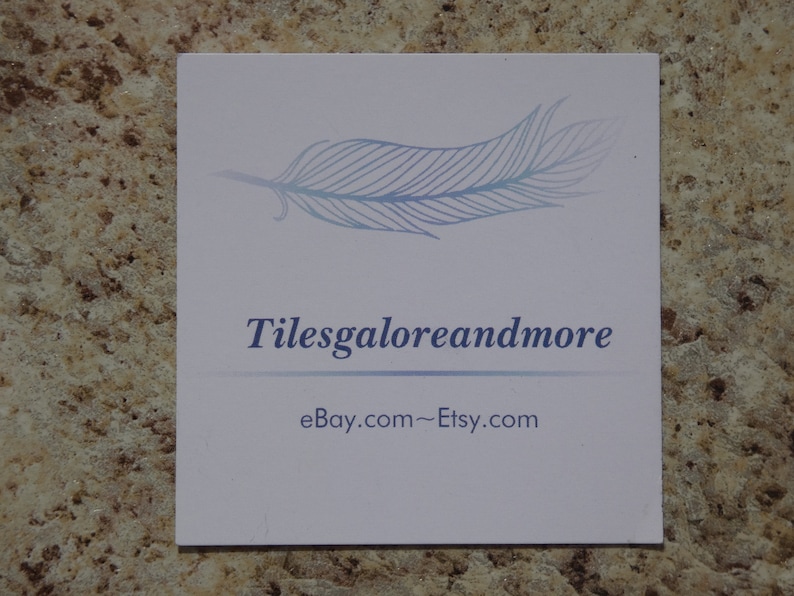 May include: A square, white card with the text "Tilesgaloreandmore" in blue, along with a feather graphic. The card also displays "ebay.com~Etsy.com" in a smaller font.