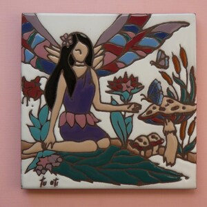 May include: Square ceramic tile featuring a fairy with black hair, a purple dress, and colorful wings. The fairy is seated near a mushroom, flowers, and butterflies. The artwork has a whimsical, fantasy theme.