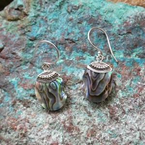 May include: A pair of silver earrings with iridescent abalone shell accents. The earrings have a simple, elegant design and are perfect for everyday wear.