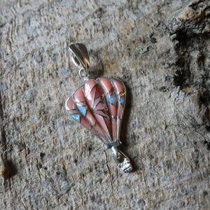 May include: A silver pendant shaped like a hot air balloon, featuring inlaid segments of pink stone and iridescent blue opal. The pendant includes a silver bail at the top and a small silver basket structure at the bottom of the balloon design.
