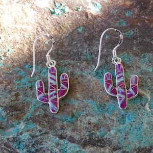 May include: Silver cactus earrings with a magenta and turquoise inlay design. The earrings feature a hook closure and a detailed, Southwestern-inspired aesthetic. The earrings are a unique accessory.
