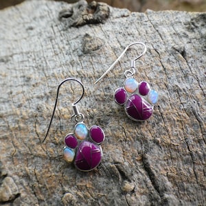 May include: A pair of silver dangle earrings with a purple paw print design. Each paw print is accented with white opal stones.