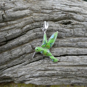 May include: A green and blue hummingbird pendant made of sterling silver. The hummingbird is in flight with its wings spread out. The pendant is a beautiful piece of jewelry that would make a great gift for any bird lover.