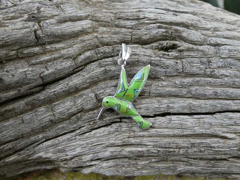 May include: A green and blue hummingbird pendant made of sterling silver. The hummingbird is in flight with its wings spread out. The pendant is a beautiful piece of jewelry that would make a great gift for any bird lover.