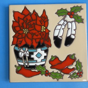 May include: A ceramic tile with a red poinsettia plant in a black and white patterned pot, two red chili peppers, and a pair of white and black feathers with green holly leaves.