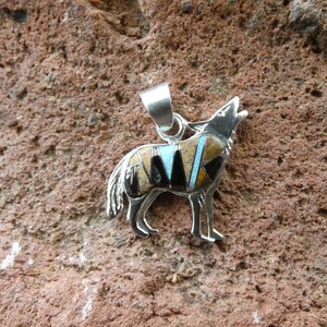 May include: Sterling silver pendant featuring a howling wolf design. The wolf is inlaid with turquoise, black onyx, and tiger's eye stones.