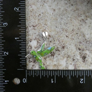 May include: A green and blue hummingbird pendant with silver accents. The pendant is about 1 inch long and is shown next to a ruler.