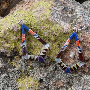 May include: A pair of geometric dangle earrings with a silver hook. The earrings are made of inlaid stone in shades of blue, red, brown, and white.