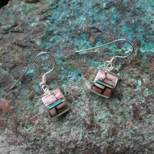 May include: A pair of silver dangle earrings featuring a curved rectangular inlay design. The inlay consists of smooth pink, light green, and black segments arranged in a geometric grid pattern. Each earring hangs from a simple silver hook wire.