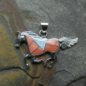 May include: A silver pendant shaped like a running horse, featuring inlaid segments of smooth, light coral-colored stone and a single triangular piece of iridescent white opal-like material, finished with a polished silver bail at the top.