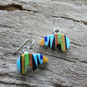 Peut inclure: Une paire de boucles d'oreilles en argent sterling avec des pendentifs en forme d'ours incrustés de pierres turquoise, noires, jaunes, orange et vertes.