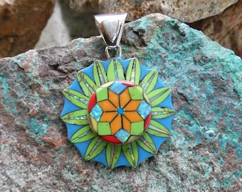 May include: A silver pendant with a colorful mosaic design. The pendant features a central flower with orange, yellow, green, blue, and red petals. The flower is surrounded by a ring of green leaves.