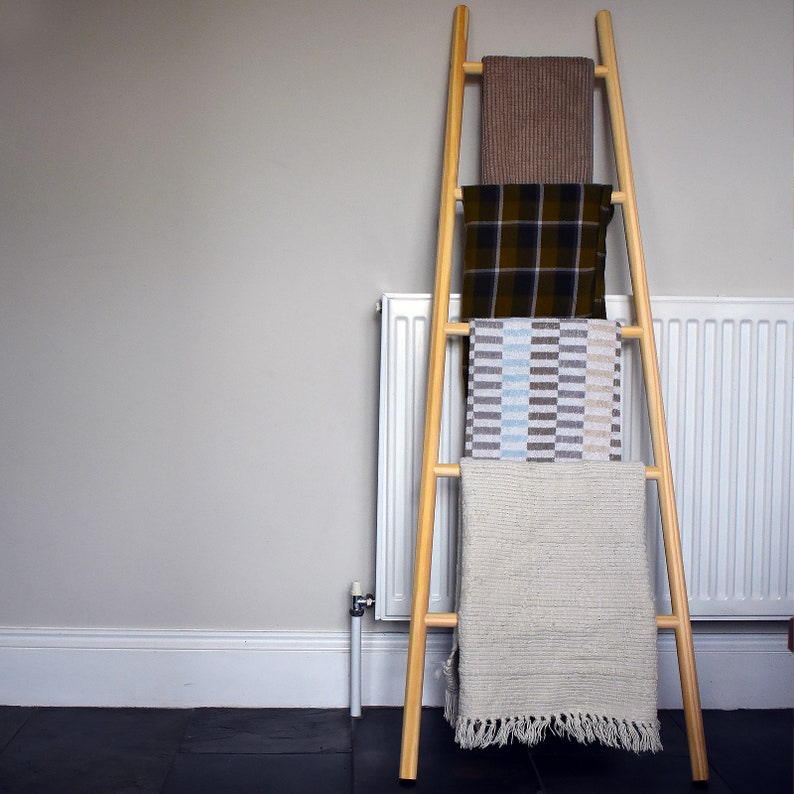 May include: A wooden ladder with four shelves, each holding a different patterned throw blanket. The blankets are brown, black and white plaid, blue and white striped, and white.