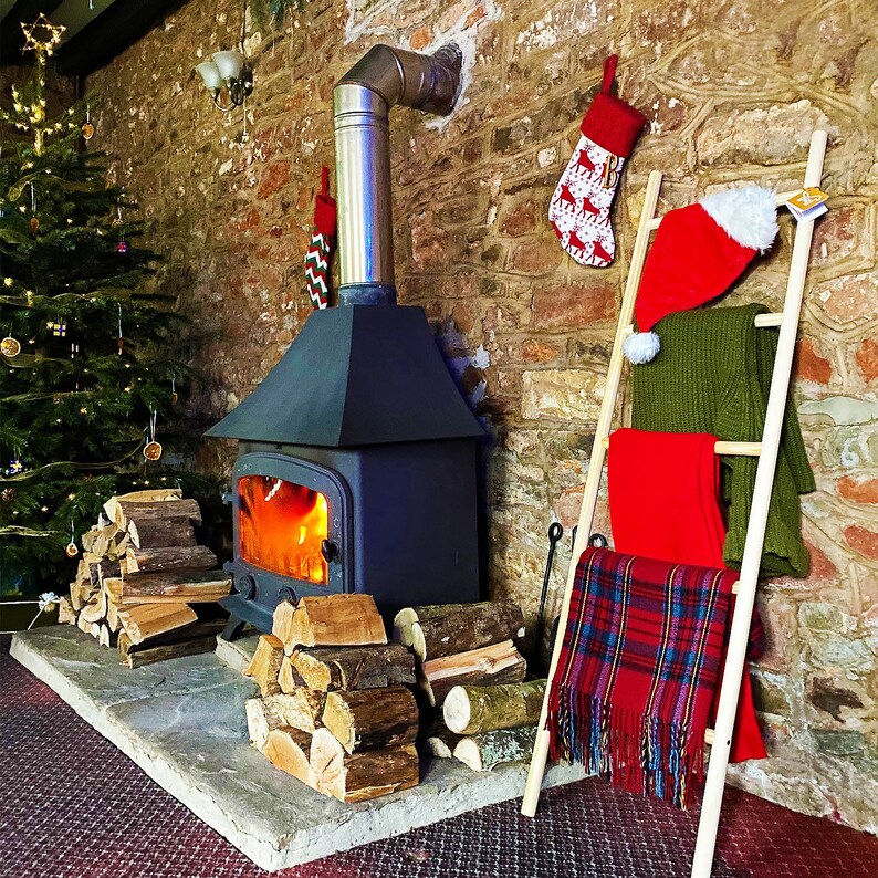 May include: A wood burning fireplace with a black metal stove and a brick chimney. The fireplace is decorated with Christmas stockings and a ladder with blankets and a Santa hat.