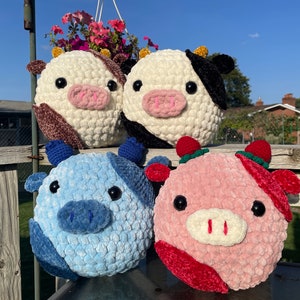 May include: Four crocheted stuffed animals in the shape of cows. The cows are different colors: brown and white, black and white, blue and white, and pink and red.