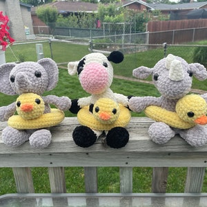 May include: Three crocheted stuffed animals, an elephant, a cow, and a rhinoceros, each holding a yellow rubber ducky.