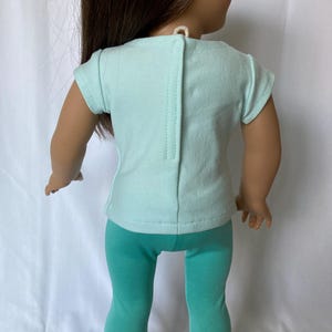 Puede incluir: Una mu&ntilde;eca vestida con una camiseta de color verde azulado claro y leggings a juego. La camiseta tiene un cierre de botones en la espalda. Los zapatos de la mu&ntilde;eca tienen detalles en negro y rosa. El conjunto est&aacute; dise&ntilde;ado para una mu&ntilde;eca.