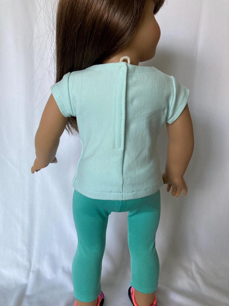 Puede incluir: Una mu&ntilde;eca vestida con una camiseta de color verde azulado claro y leggings a juego. La camiseta tiene un cierre de botones en la espalda. Los zapatos de la mu&ntilde;eca tienen detalles en negro y rosa. El conjunto est&aacute; dise&ntilde;ado para una mu&ntilde;eca.