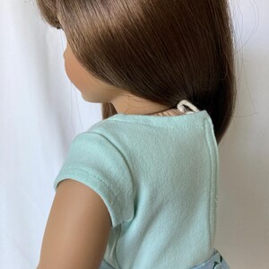 Puede incluir: Una mu&ntilde;eca con cabello casta&ntilde;o largo, que lleva una camiseta de manga corta azul claro y una falda floral azul. La falda tiene un estampado floral blanco. La mu&ntilde;eca est&aacute; mirando hacia la izquierda, con el lado de su cara visible.