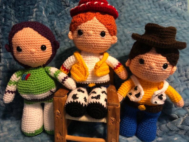 K&ouml;nnte beinhalten: Drei geh&auml;kelte Puppen, inspiriert von Charakteren aus der Zeichentrickfilmreihe Toy Story. Die Puppen umfassen Buzz Lightyear in Gr&uuml;n und Wei&szlig;, Jessie in einem Cowgirl-Outfit und Woody in einem Cowboy-Outfit.