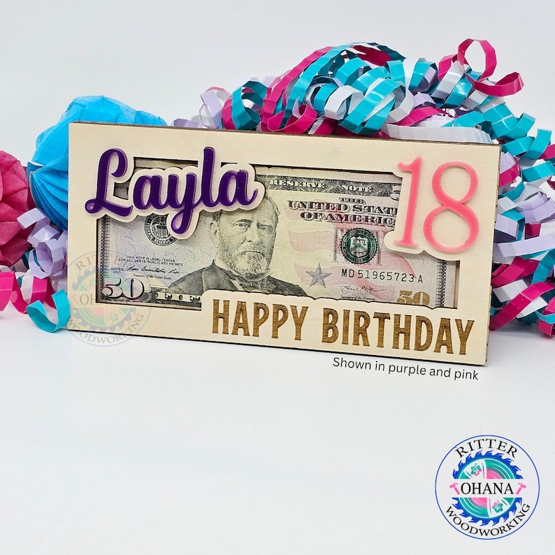 May include: Wooden money holder with a slot for a bill, personalized with the name "Layla" in purple and the number "18" in pink. The text "Happy Birthday" is engraved on the front.