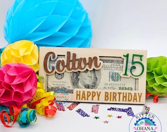 May include: A wooden money holder with the name "Cotton" and the number "15" in green. The holder has a slot for a bill and says "Happy Birthday".
