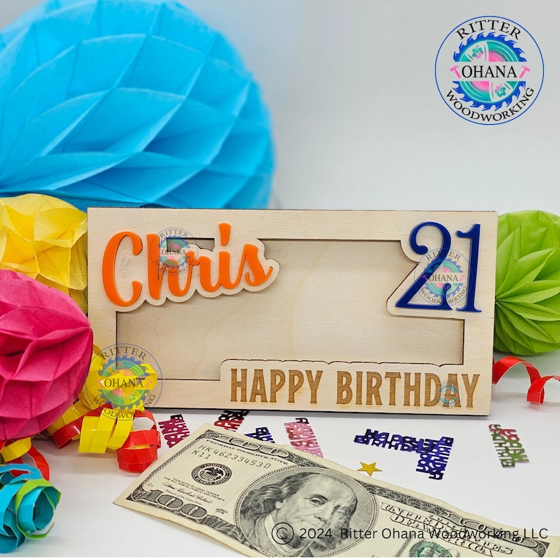 May include: A wooden picture frame with a cutout for a photo. The frame is decorated with the name "Chris" in orange letters and the number "21" in blue letters. The words "Happy Birthday" are engraved on the bottom of the frame.