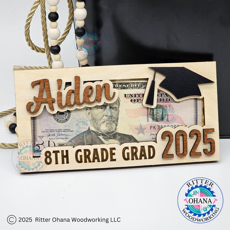 Puede incluir: Un portamonedas de madera con un recorte de gorro de graduaci&oacute;n. El portamonedas est&aacute; personalizado con el nombre "Aiden" y el texto "8th Grade Grad 2025".