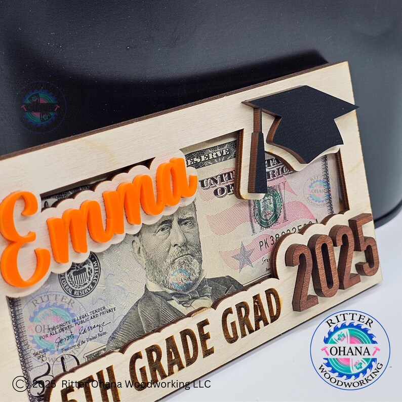 Puede incluir: Un marco de madera con un recorte de gorro de graduaci&oacute;n, un billete de d&oacute;lar y el texto "Emma 5th Grade Grad 2025". El marco est&aacute; hecho por Ritter Ohana Woodworking LLC.