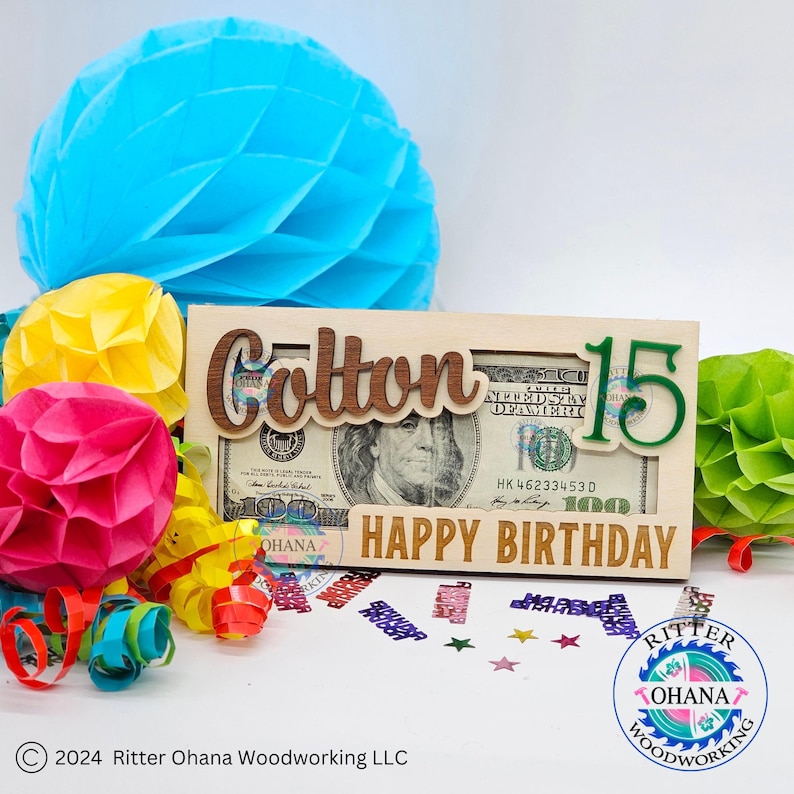 May include: A wooden money holder with the name "Cotton" and the number "15" in green. The holder has a slot for a bill and says "Happy Birthday".