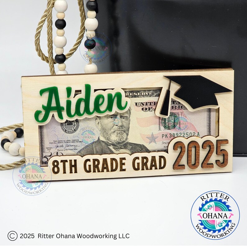 Puede incluir: Un portamonedas de madera para la graduaci&oacute;n de 8&ordm; grado con una ranura para un billete. El portamonedas est&aacute; decorado con un nombre verde "Aiden", un gorro de graduaci&oacute;n y el a&ntilde;o "2025".