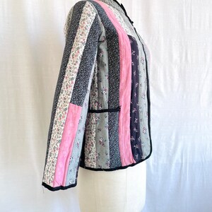 May include: A quilted jacket with a mandarin collar and long sleeves. The jacket is made of patchwork fabric in shades of pink, grey, and black with floral patterns.