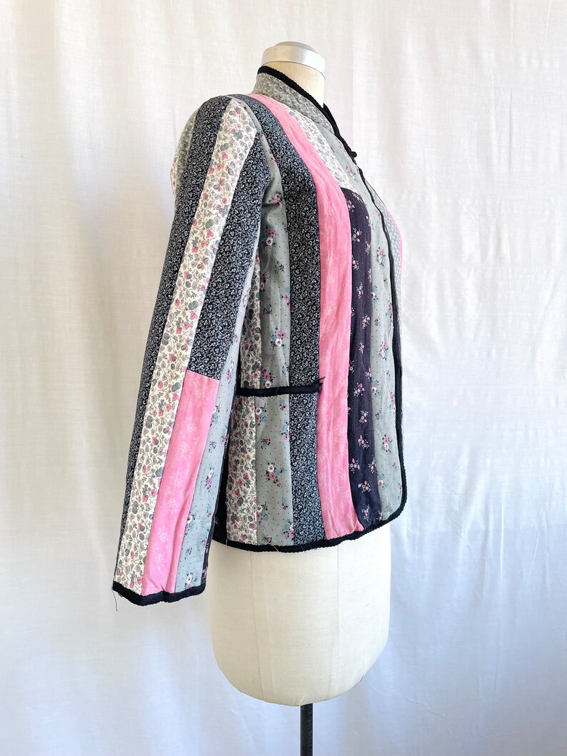 May include: A quilted jacket with a mandarin collar and long sleeves. The jacket is made of patchwork fabric in shades of pink, grey, and black with floral patterns.