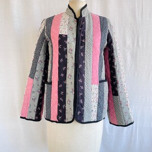 May include: A quilted jacket with a black zip and a patchwork design featuring pink, black and grey floral fabric.