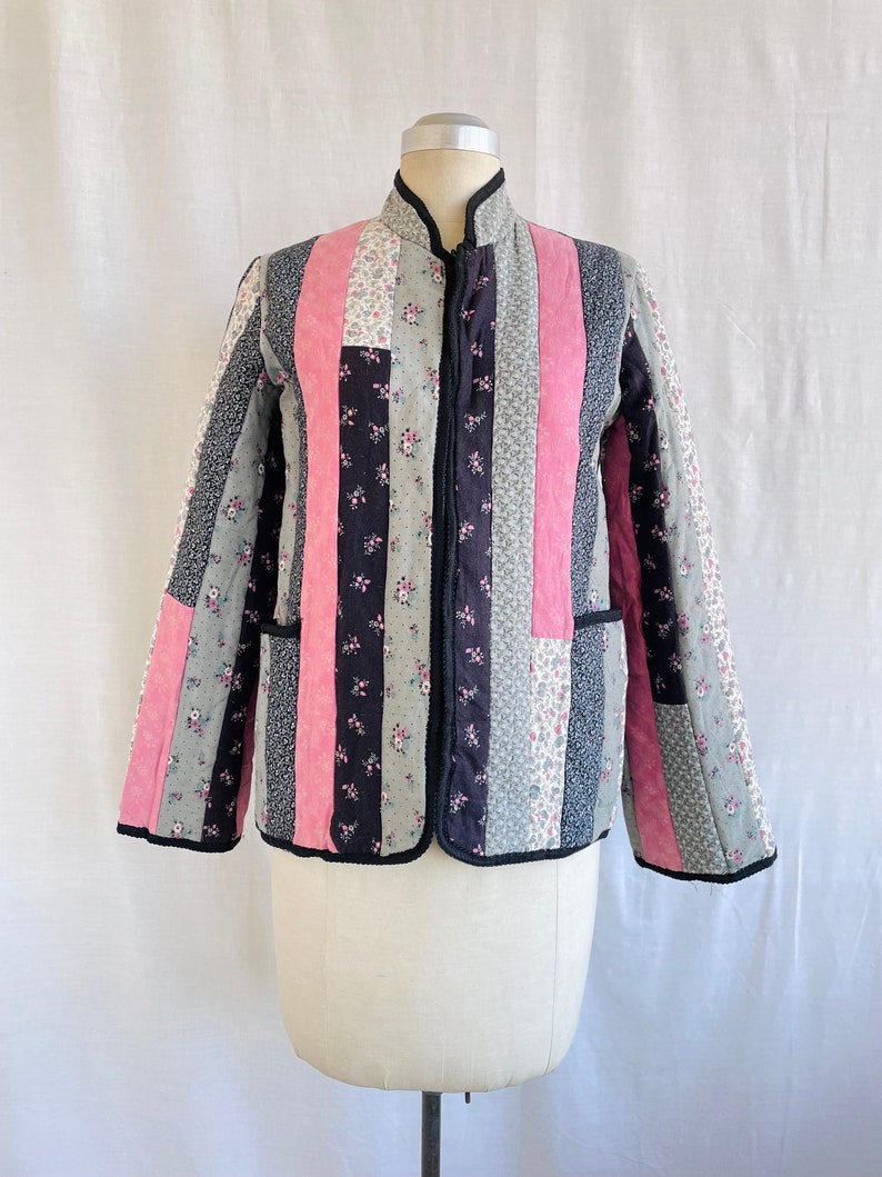 May include: A quilted jacket with a black zip and a patchwork design featuring pink, black and grey floral fabric.