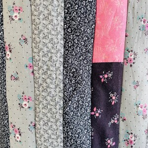 May include: A close-up of a patchwork quilt with vertical stripes of different floral patterns in shades of grey, black, and pink.
