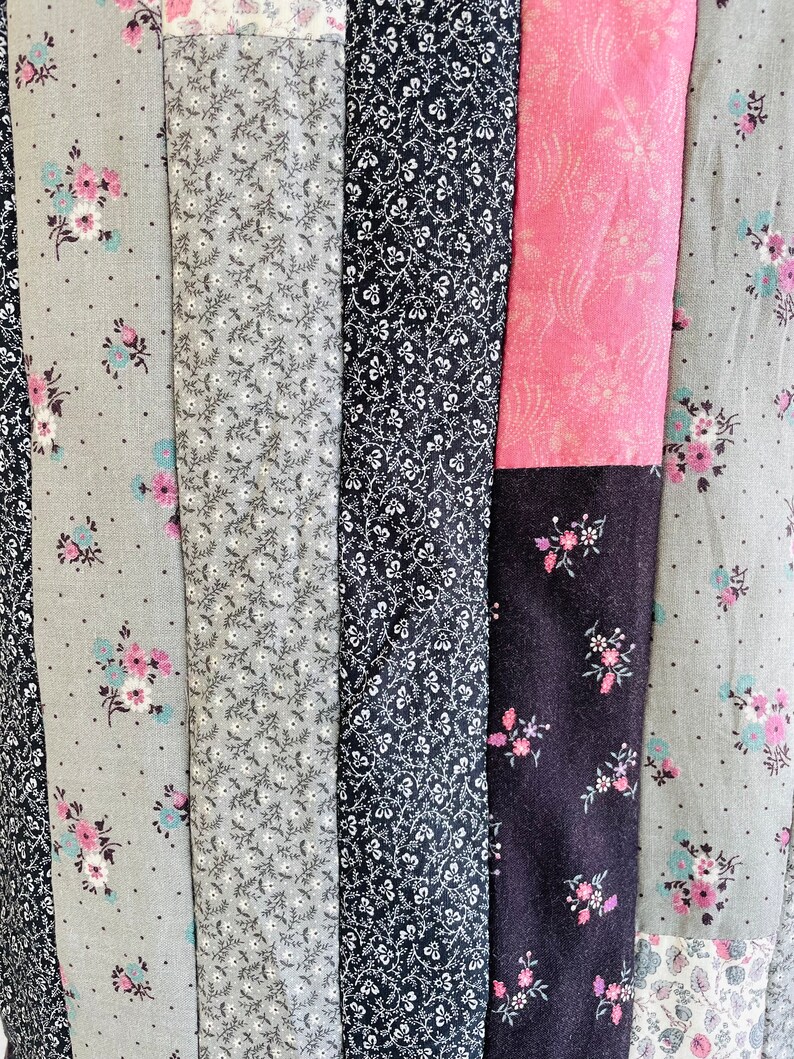 May include: A close-up of a patchwork quilt with vertical stripes of different floral patterns in shades of grey, black, and pink.