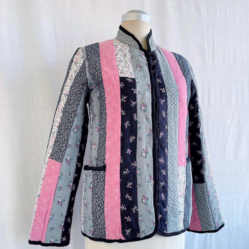 May include: A quilted jacket with a mandarin collar and a zip closure. The jacket is made of patchwork fabric in shades of pink, blue, and black with floral patterns.