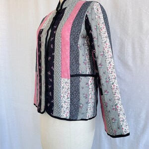 May include: A quilted jacket with a black, pink and floral print. The jacket has a mandarin collar and a button closure.