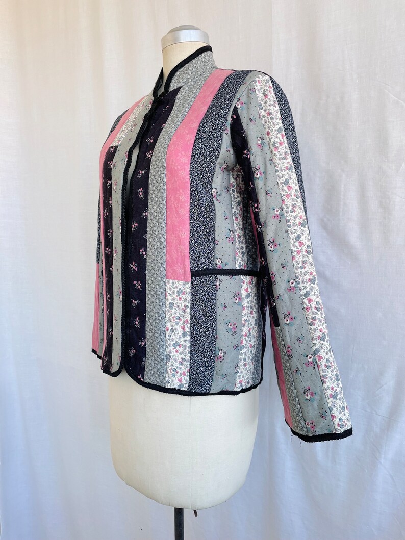 May include: A quilted jacket with a black, pink and floral print. The jacket has a mandarin collar and a button closure.