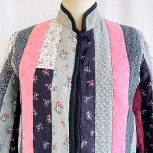May include: A quilted jacket with a mandarin collar and a button fastening. The jacket is made from patchwork fabric in shades of pink, black and grey with floral patterns.