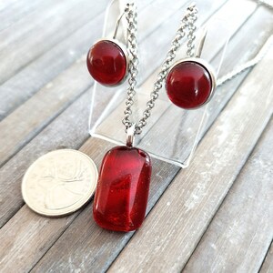 Peut inclure: Un ensemble de collier et boucles d'oreilles en verre rouge avec une chaîne en argent. Le pendentif est rectangulaire et les boucles d'oreilles sont rondes.