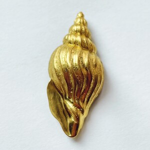 May include: A gold-colored seashell pendant with a detailed, textured surface. The shell is shaped like a spiral and has a pointed tip.