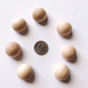 Op de afbeelding: Zeven onafgewerkte houten bollen gerangschikt rond een munt. De bollen zijn lichtbruin en glad, met zichtbare houtnerf. De munt is zilverkleurig en toont het profiel van George Washington.